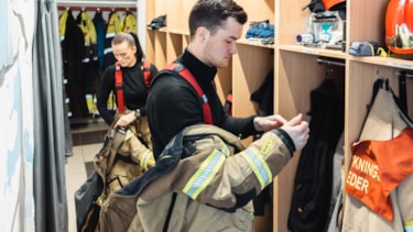 To brannkonstabler kler på seg røykdykkerutstyr i garderoben